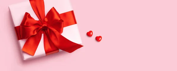 Caja de regalo rosa con lazo rojo y dos corazones sobre fondo rosa. Vista superior. Puesta plana. —  Fotos de Stock