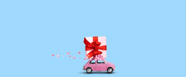 Carro rosa com caixa de presente em um telhado com flores em um fundo azul. — Fotografia de Stock