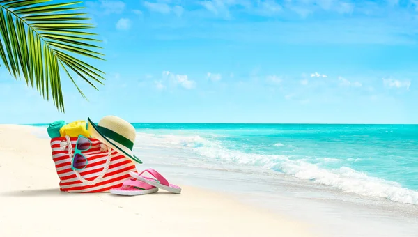 Sommer-Strandtasche und Accessoires am Sandstrand und azurblaues Meer im Hintergrund — Stockfoto