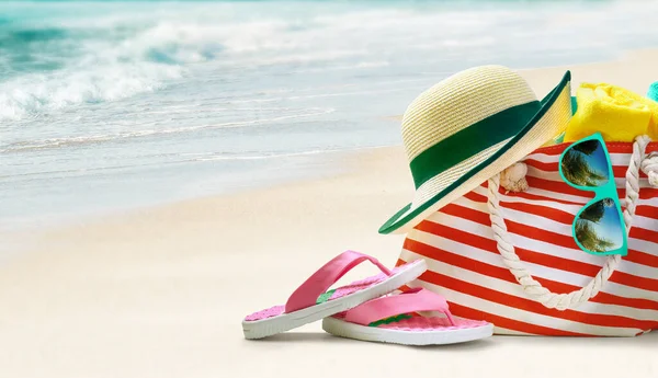 Καλοκαιρινή τσάντα θαλάσσης και αξεσουάρ - καπέλο ήλιου, σαγιονάρες και γυαλιά ηλίου στην αμμώδη παραλία. — Φωτογραφία Αρχείου