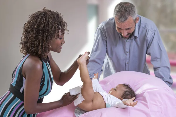 Baby Changing. Mãe amorosa mudando fralda de sua filha bebê., Criança pequena, menina na mesa de vestir, enquanto o pai está olhando alegre — Fotografia de Stock