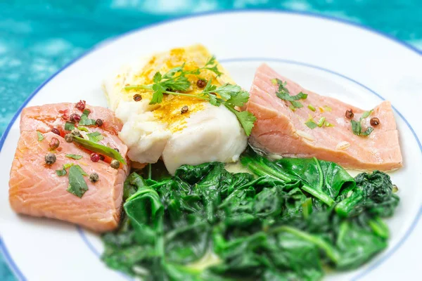 Filé de bacalhau e salmão com arroz e espinafre. Bife de peixe. Salmão de limão na placa branca no fundo de madeira — Fotografia de Stock