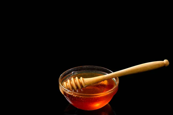 Honey in bowl with wood stick isolated on black background — Stock Photo, Image