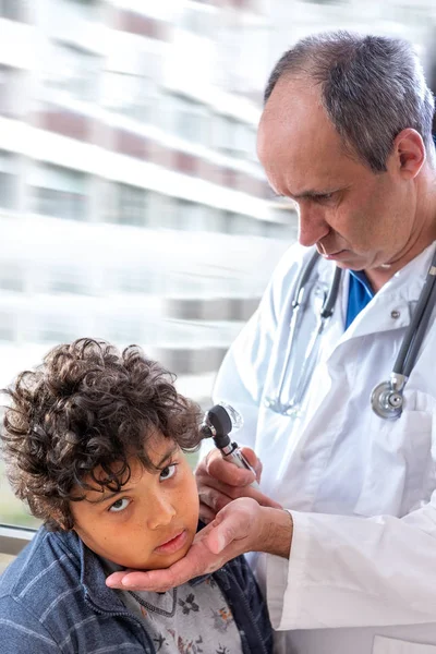 Smiling doctor examining little boys ears with otoscope at hs offciee — Stok Foto