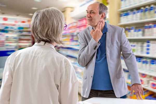 建议和一致性概念：药剂师在药房与客户交谈，男性喉咙痛 — 图库照片