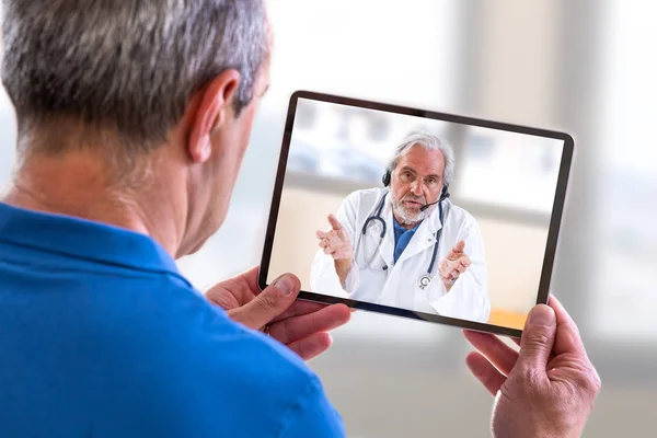 Concepto de telemedicina, Doctor sentado en el hospital, con portátil, teniendo una llamada en línea con un paciente que muestra un dispositivo de ablet — Foto de Stock