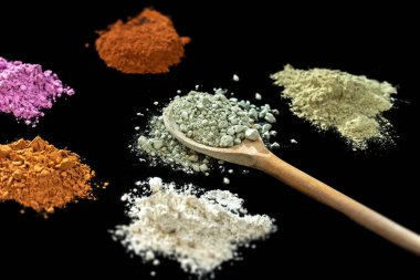 Tahta bir kaşık yüz ve vücut için kuru tıkanmış kil maskesi. Siyah arka plan üzerinde yalıtılmış