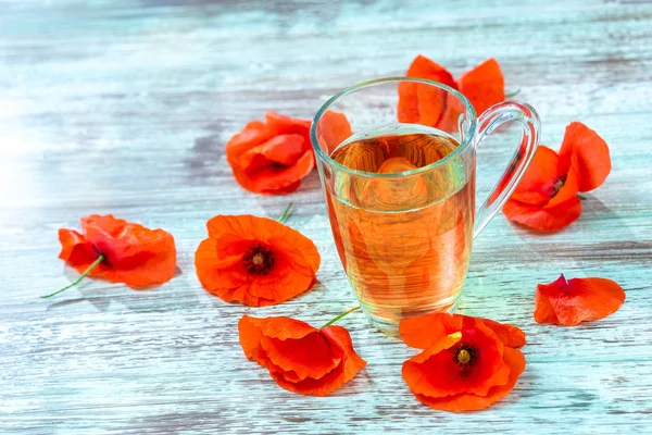 Κόκκινη παπαρούνα ποτό λουλουδιών σε γυάλινο κούπα σε ξύλινο φόντο. Έννοια της υγιεινής διατροφής. — Φωτογραφία Αρχείου