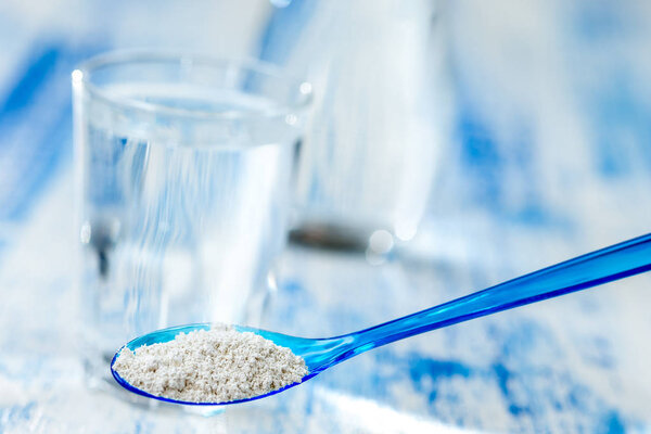 A drink of clay , Spoon of white clay in glass of fresh water blue background