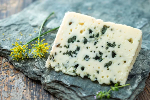 Französischer Blauschimmelkäse Roquefort, hergestellt aus Schafsmilch in den Höhlen von Roquefort-sur-Soulzon mit Trauben auf grauem Stein — Stockfoto