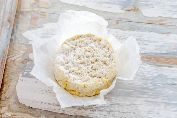 Camembert-Käse auf weißem Papier und rustikalem weißen Holzhintergrund. Ansicht von oben — Stockfoto