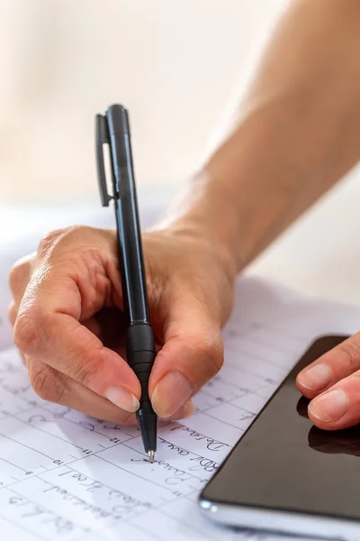 Hand van zakelijke vrouw houden zwarte pen en smartphone op werkplek iets schrijven in dagboek close-up — Stockfoto