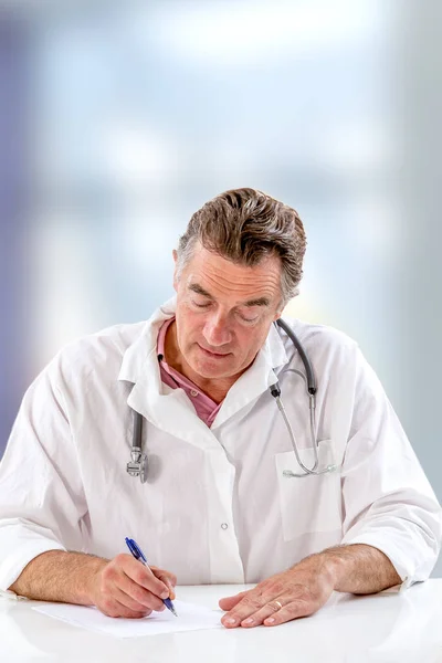 Médico escrevendo formulário de prescrição enquanto sentado na mesa branca no hospital, vista close-up . — Fotografia de Stock
