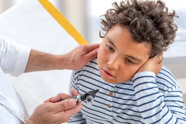 若い十代の若者は耳が痛い。中耳炎に苦しむ小さな男の子は医者に相談する — ストック写真