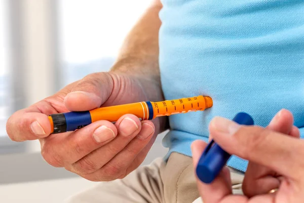 Man die zichzelf een insuline injectie geeft met een insuline pen om diabetes thuis of op kantoor te behandelen — Stockfoto