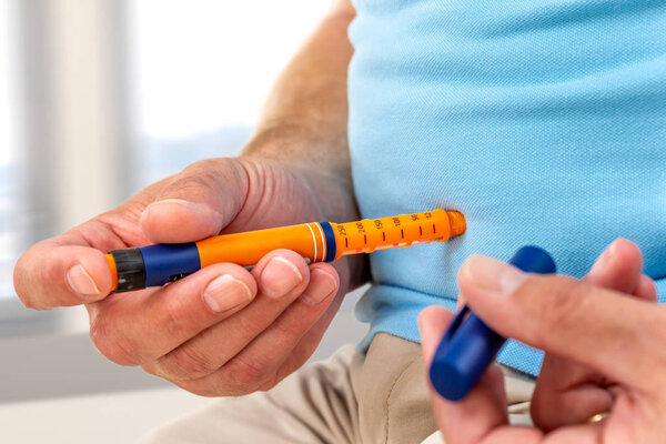Man giving himself an insulin injection with an insulin pen to treat diabetes at home or office