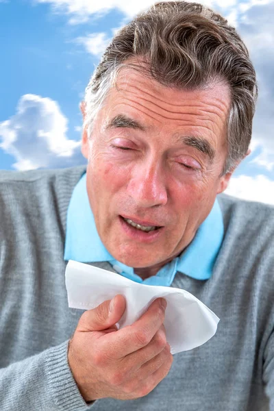 Senior Man with a common cold is blowing his nose with a tissue — Stock Photo, Image