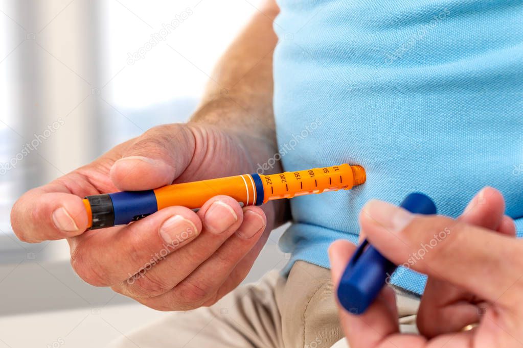 Man giving himself an insulin injection with an insulin pen to treat diabetes at home or office