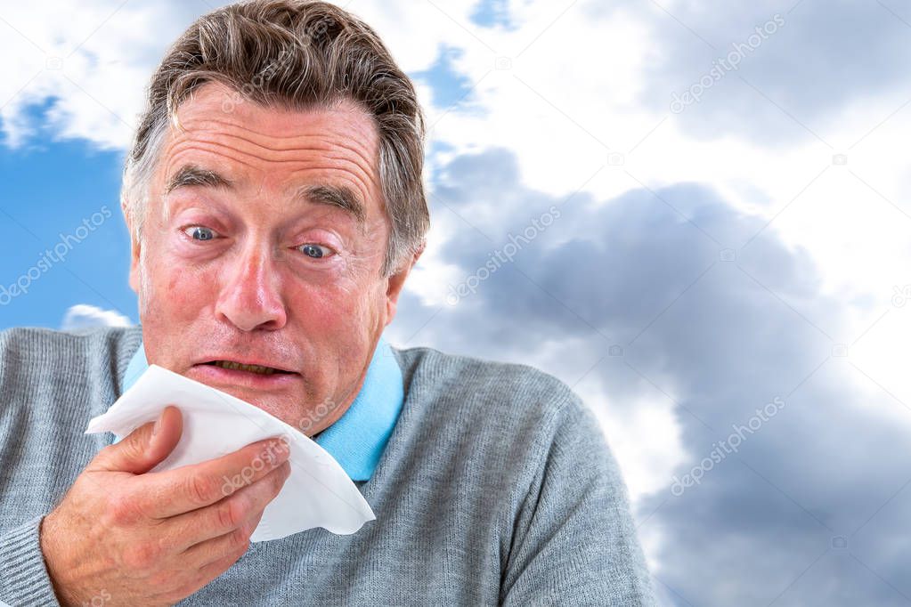 Senior Man with a common cold is blowing his nose with a tissue