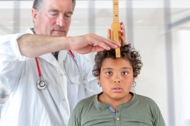 Bir doktor tıbbi muayene sırasında bir çocuğun boyunu ölçer. 12-14 yaş arası.