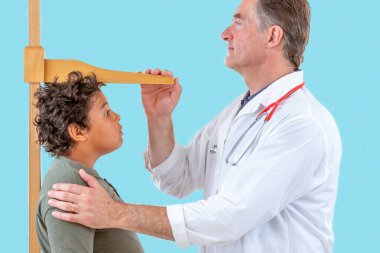 Bir doktor tıbbi muayene sırasında bir çocuğun boyunu ölçer. 12-14 yaş arası.