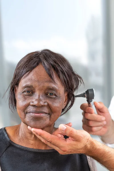 Doctor sosteniendo otoscopio y examinando la oreja de una mujer africana mayor . — Foto de Stock