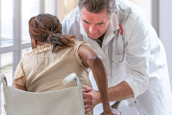 Vriendelijke blanke arts helpt Afrikaanse senior vrouw opstaan uit rolstoel — Stockfoto