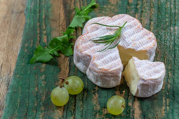 Queso francés Saint Albray, rebanadas en tabla de cortar de madera, estilo rústico con uvas —  Fotos de Stock