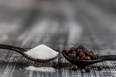 Deniz tuzu ve karabiber kaplı tahta kaşıklar beyaz ve siyah arkaplanda kopya alanı.