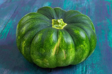 Yuvarlak, canlı yeşil bir balkabağı desenli, renkli bir yüzeye yerleştirilir. Pürüzsüz derisi, zengin ve taze bir hasat sunan yeşilin çeşitli tonlarına sahiptir..