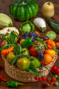 Canlı bir sebze çeşidi dokuma sepetini doldurur, olgunlaşmış domatesler, biberler, patlıcanlar ve çeşitli yeşillikler sergilenir..