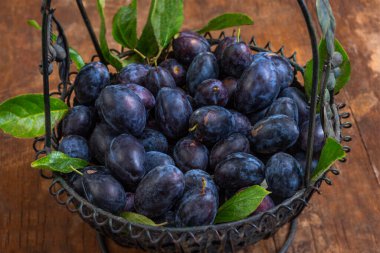 Olgunlaşmış eriklerle dolu bir köy sepeti ahşap bir masanın üzerinde duruyor. Eriklere yeşil yapraklar eşlik ediyor, tazeliklerini sergiliyorlar. Ayarlar sıcak ve davetkar bir atmosfer olduğunu gösteriyor..