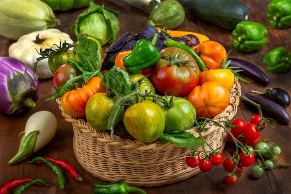 Domatesler, biberler ve patlıcanlar dahil taze sebzelerle dolu dokuma sepeti, sıcak aydınlatmada sade ahşap bir masa üzerine dizilmiştir..