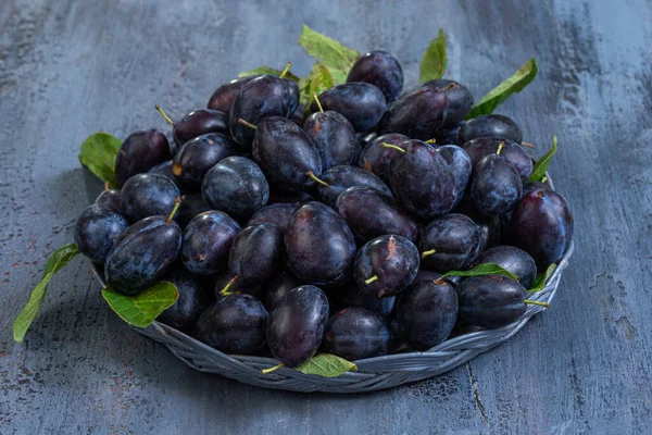 Bir dokuma sepeti taze, koyu eriklerle doludur, zengin renkleri ve yeşil yaprakları sergilenir. Bu meyve düzenlemesi kırsal alanda mevsimsel hasat vurguluyor.