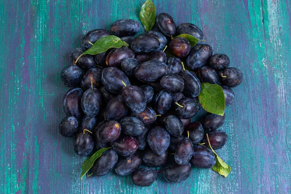 Canlı bir taze erik yığını eskimiş ahşap bir yüzeyde duruyor, koyu mor renklerini ve yeşil yapraklarını sergiliyorlar. Düzenleme meyvenin doğal güzelliğini vurguluyor..