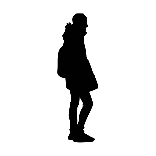 Молодой человек в теплой куртке, джинсах и кроссовках стоит. Черный силуэт выделен на белом фоне. Вид сбоку. Монохромная векторная иллюстрация молодого человека с рюкзаком. Концепция — стоковый вектор