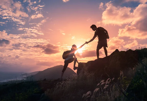 人们在日出时互相帮助爬上一座山 — 图库照片