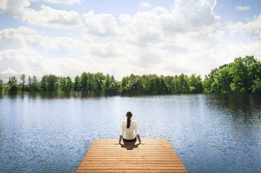 Woman sitting on a wooden dock next to lake. 