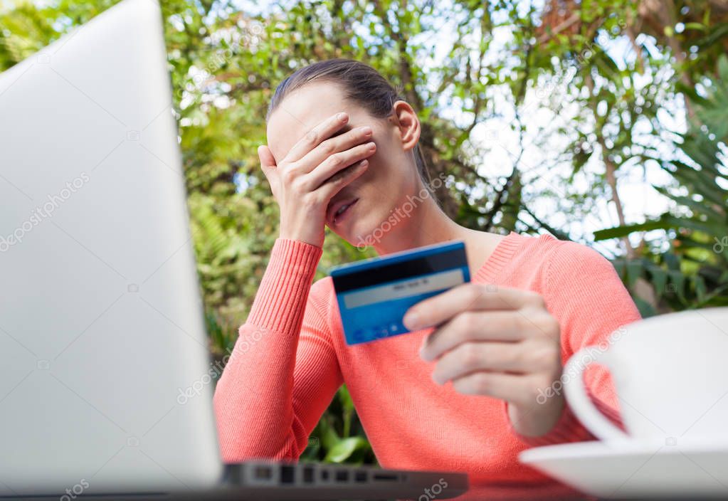 Stressed woman holding credit card for online shopping.