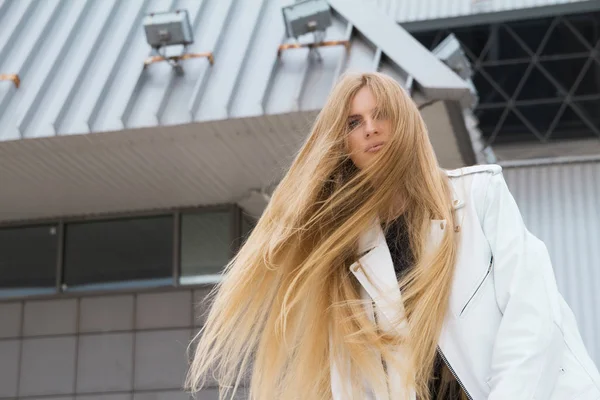 Sarışın kadın kentsel arka planda. Güzel genç kız sokakta bekleyen bir beyaz deri ceket giyiyor.