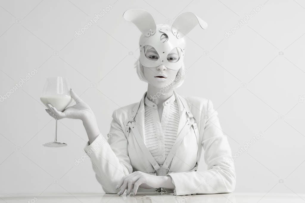 Studio fashion portrait of beautiful white lady in mask rabbit with glass of milk