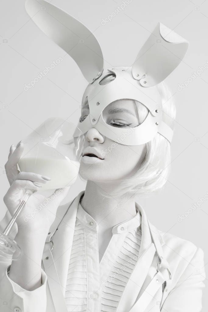 Studio fashion portrait of beautiful white lady in mask rabbit with glass of milk