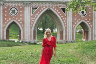 Uzun kırmızı elbiseli güzel ve zarif kız Ortaçağ Kalesi ortasında duruyor