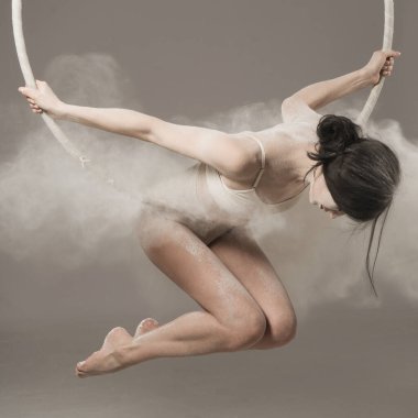 Havada jimnastik yapan taytlı, genç, ince bir kız ve beyaz tozun ellerini bulut şeklinde fırlatıyor..