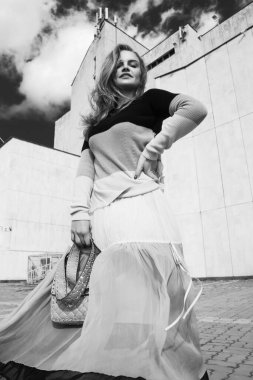 Elbise ve ceketle poz veren güzel bir kız. Elinde bir çanta, elinde siyah beyaz bir fotoğraf.