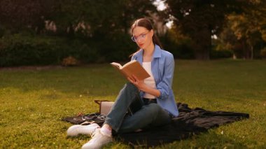 Gözlüklü genç kız kampüste ya da parkta çimenlerde oturur, kitap okur, arkadaşlarını fark eder, el sallar merhaba, güneşli ve rahatlatıcı çalışma anlarından zevk alır..