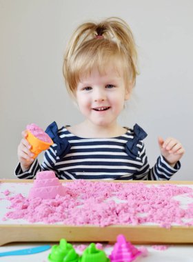 Eve erken eğitim okul geliştirme çocuk oyunu için hazırlanıyor pembe kinetik kumla oynayan küçük beyaz kız