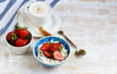 Süzme peynir çilek, fincan Cappuccino içecek çiçek ahşap arka plan masa mutfak, havlu mavi kase, kahvaltı konsepti