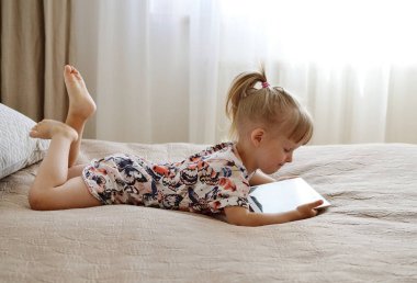 Beyaz küçük sarışın kız yatak, ev İçişleri, Modern cihaz teknolojileri İskandinav tarzında tablet oyun oynamak