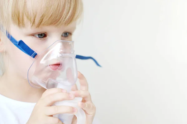 Little girl in a mask for inhalations, making inhalation with nebulizer at home inhaler on the table, indoor, sick child